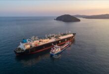 A large Avenir LNG carrier vessel docked at a busy maritime port terminal.